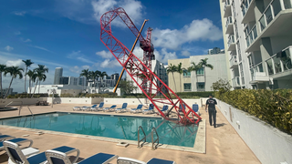 El brazo de una grúa se derrumba en la zona de la piscina de la azotea de un bloque de pisos de « Miami », mientras los trabajadores se aferran a la estructura que cuelga en el aire