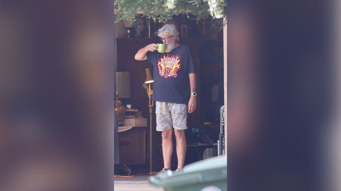 image shows Hooker standing and holding green coffee cup