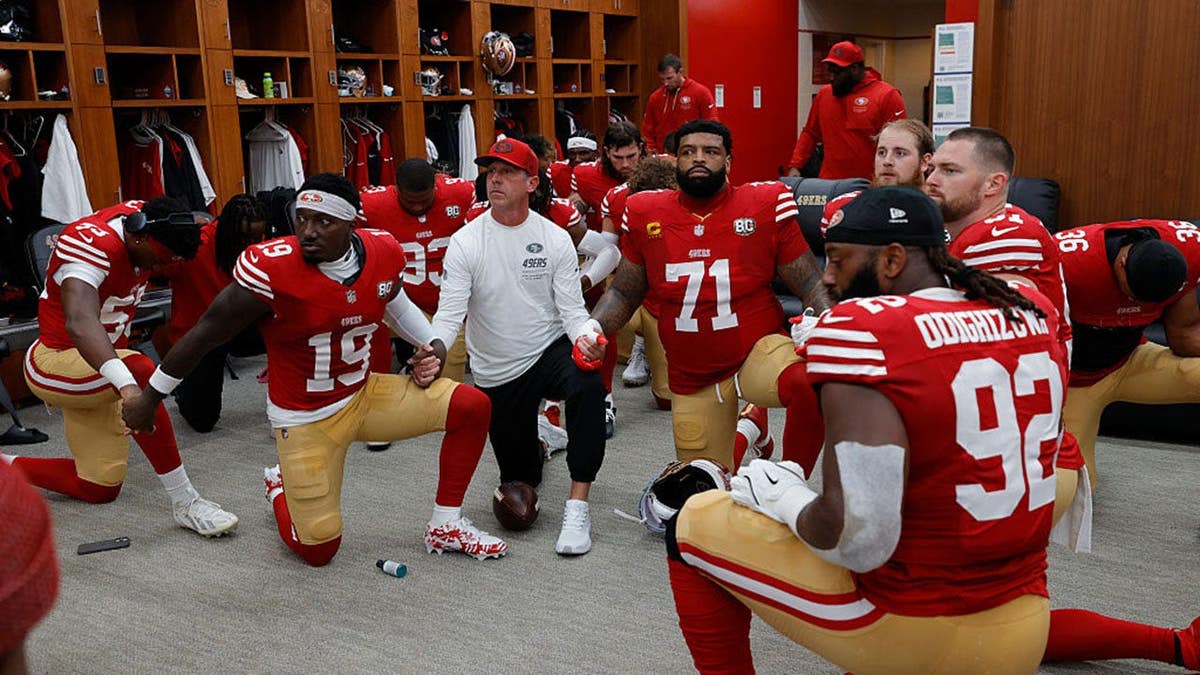 San Francisco 49ers players pray together in a locker room before a game.