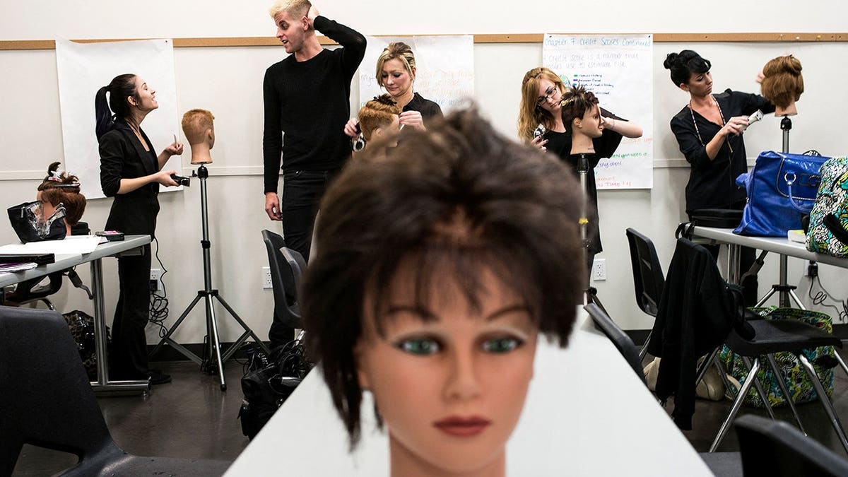 Students practice cutting hair on mannequin heads in a classroom at Paul Mitchell School.