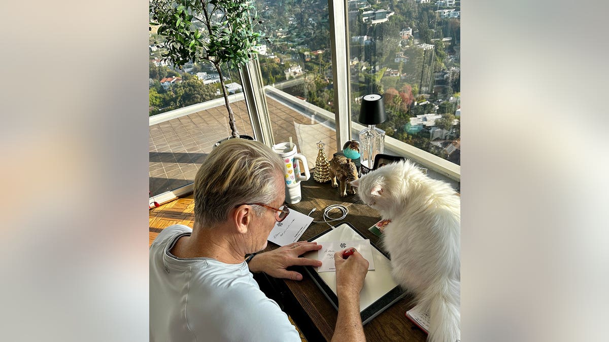 Dolph Lundgren writing a letter next to his cat.
