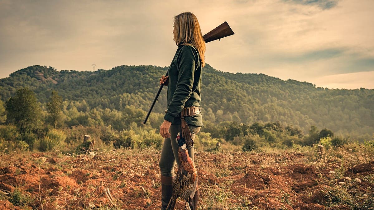 female pheasant hunter stands in open field