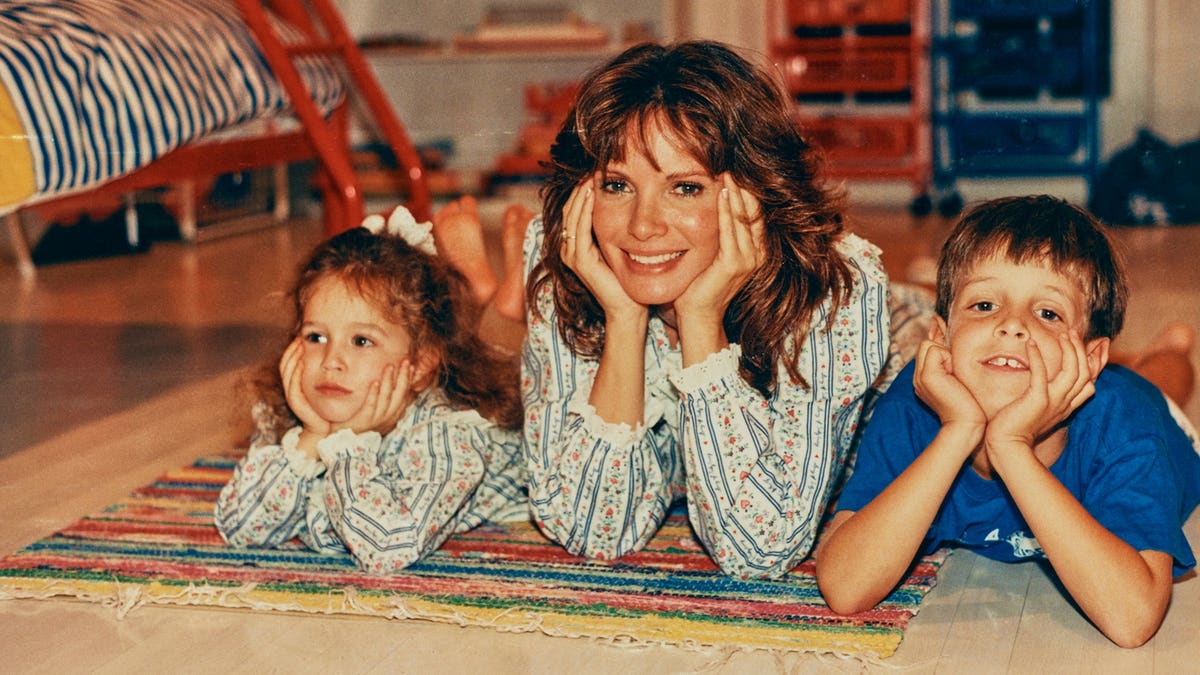 Jaclyn Smith laying on the floor with her two young children.