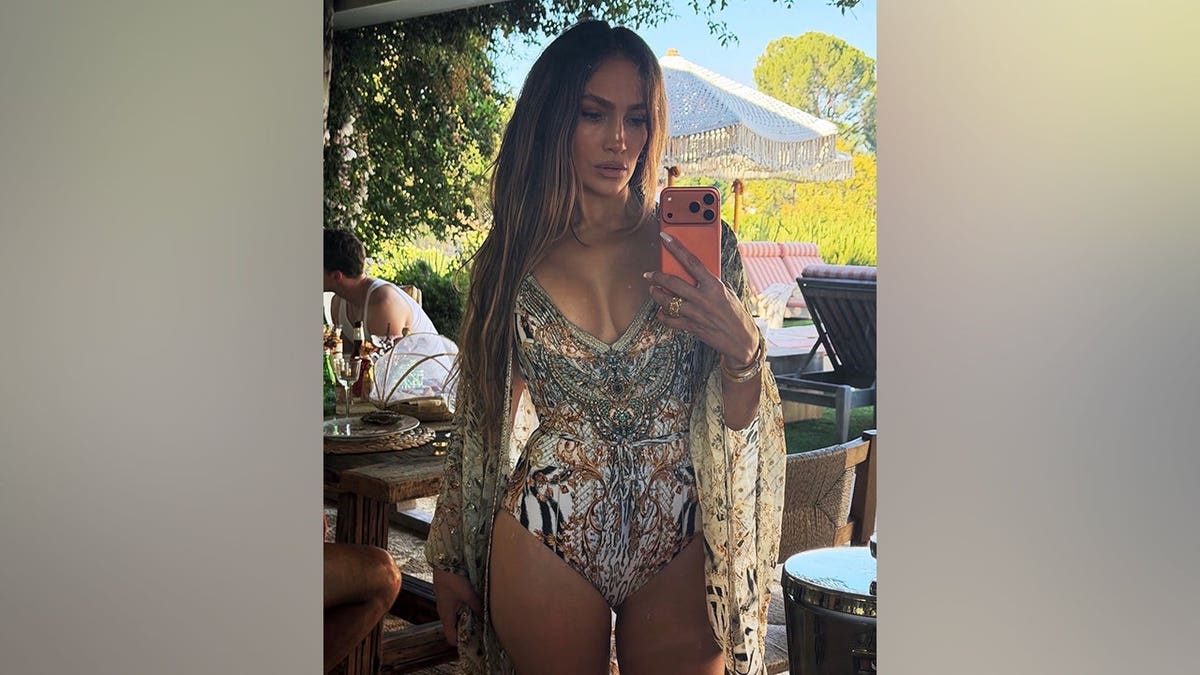 Jennifer Lopez takes a full-length mirror selfie in a patterned one-piece swimsuit and matching cover-up.
