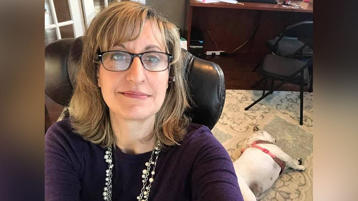 Northern Virginia real estate agent Lisa Bradford poses for a photo while seated in an office with a dog lying on the floor behind her.