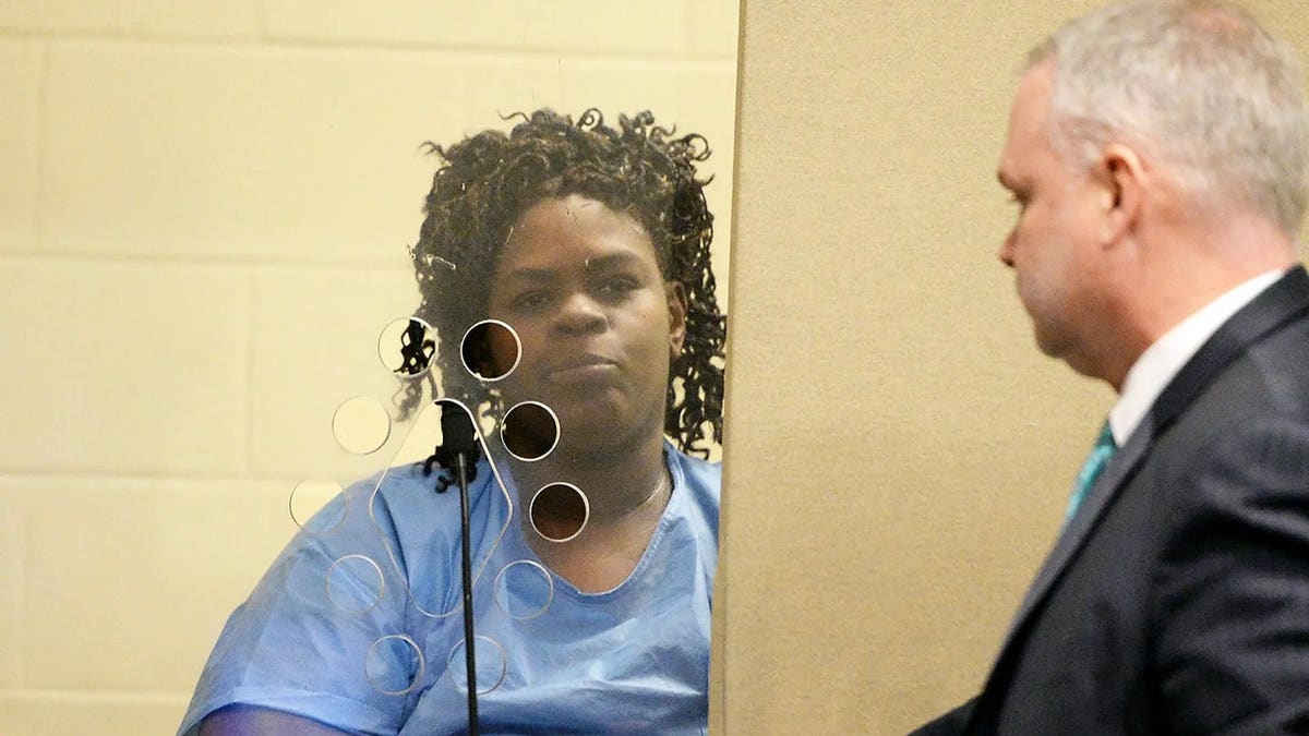 Latarsha Sanders appears in court wearing a blue jail uniform as an attorney walks past during her murder trial in Plymouth Superior Court.