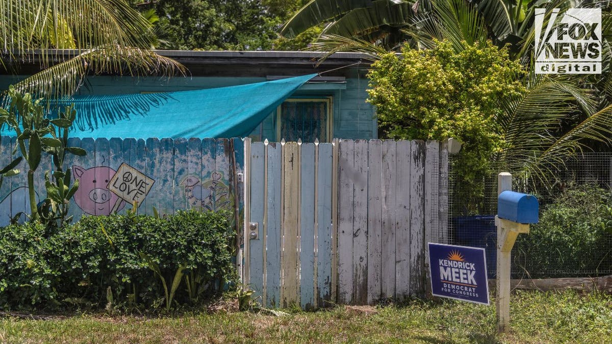 Miami property behind a weathered painted fence and tropical vegetation.