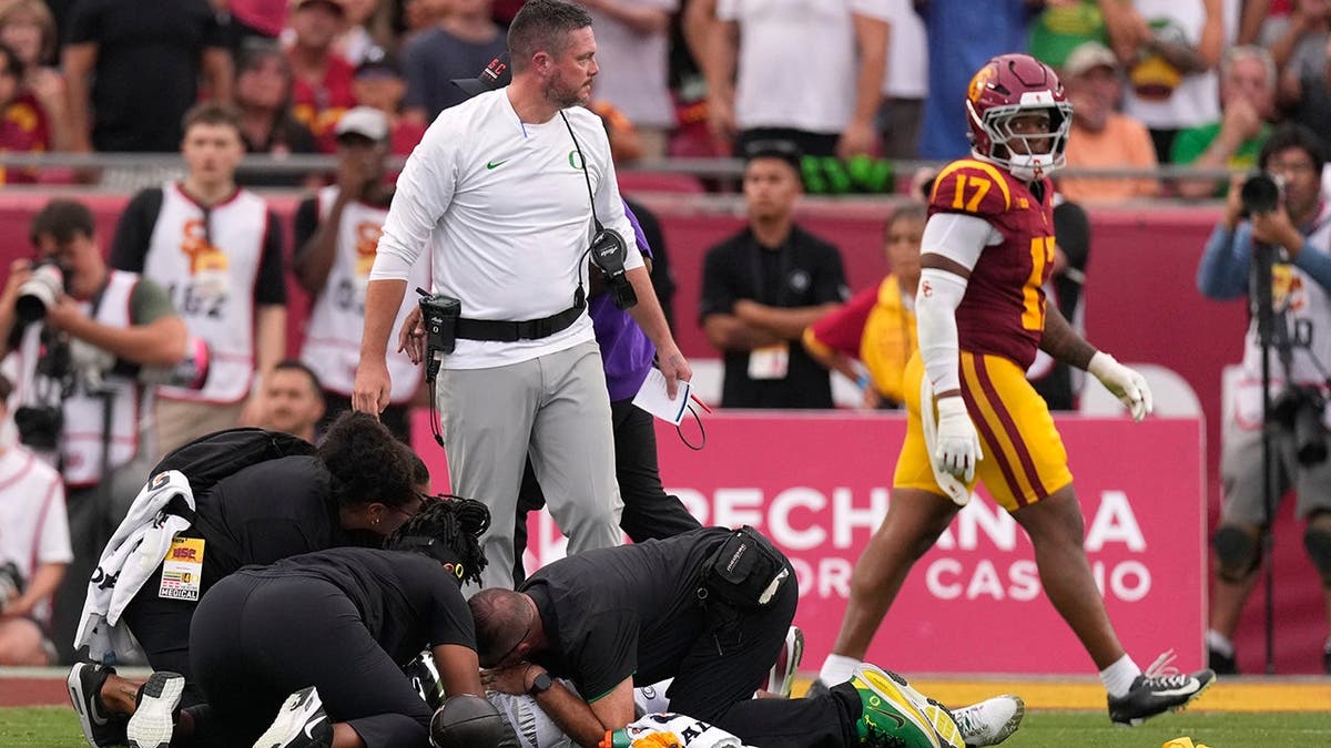 Dan Lanning stands over Dante Moore as Moore is attended to during a football game.