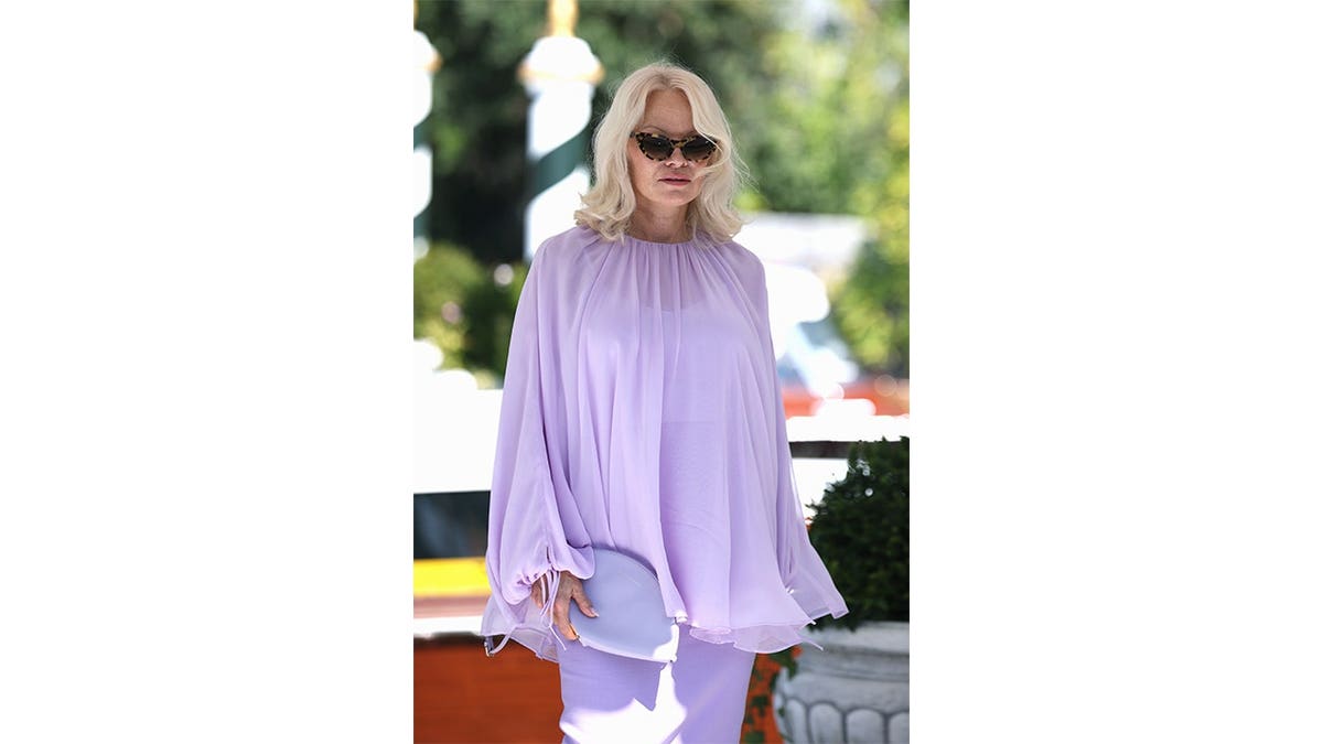 Pamela Anderson wears a lavender outfit and sunglasses while standing outdoors in Venice.