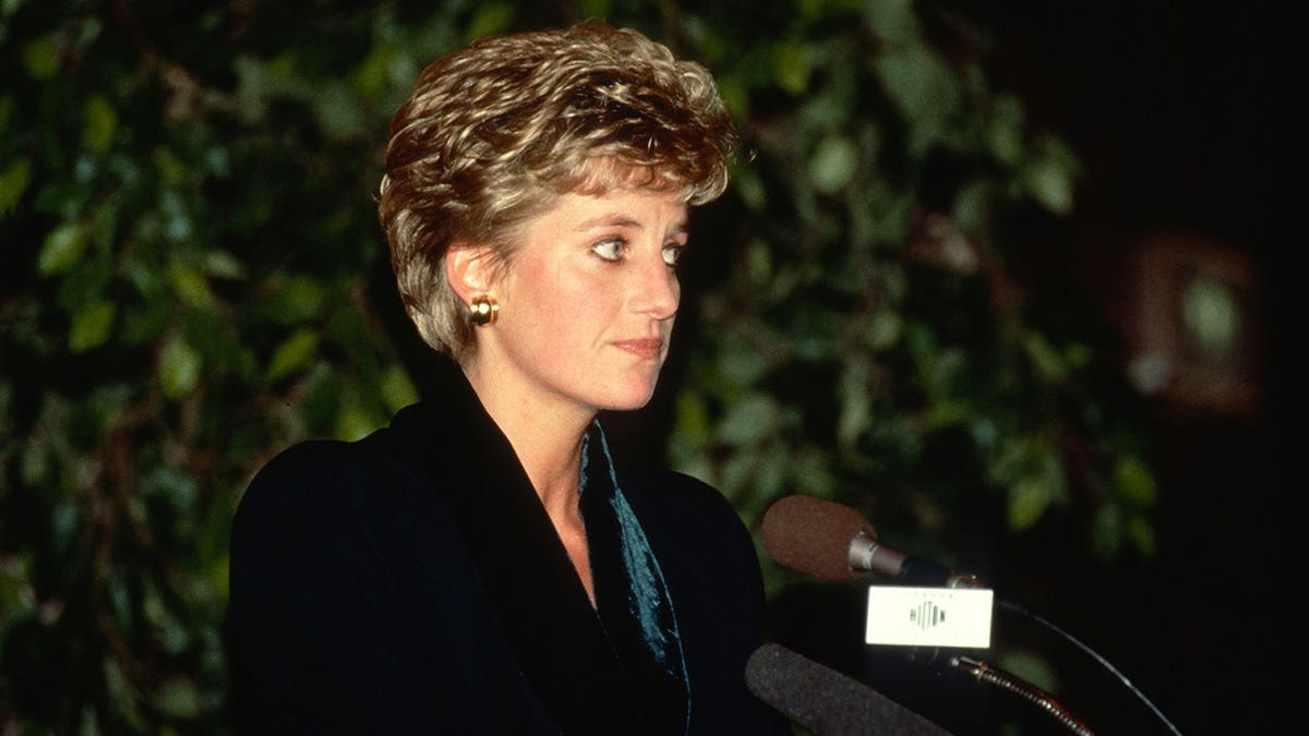 Diana, Princess of Wales, speaks at a podium wearing a green suit with velvet collar.