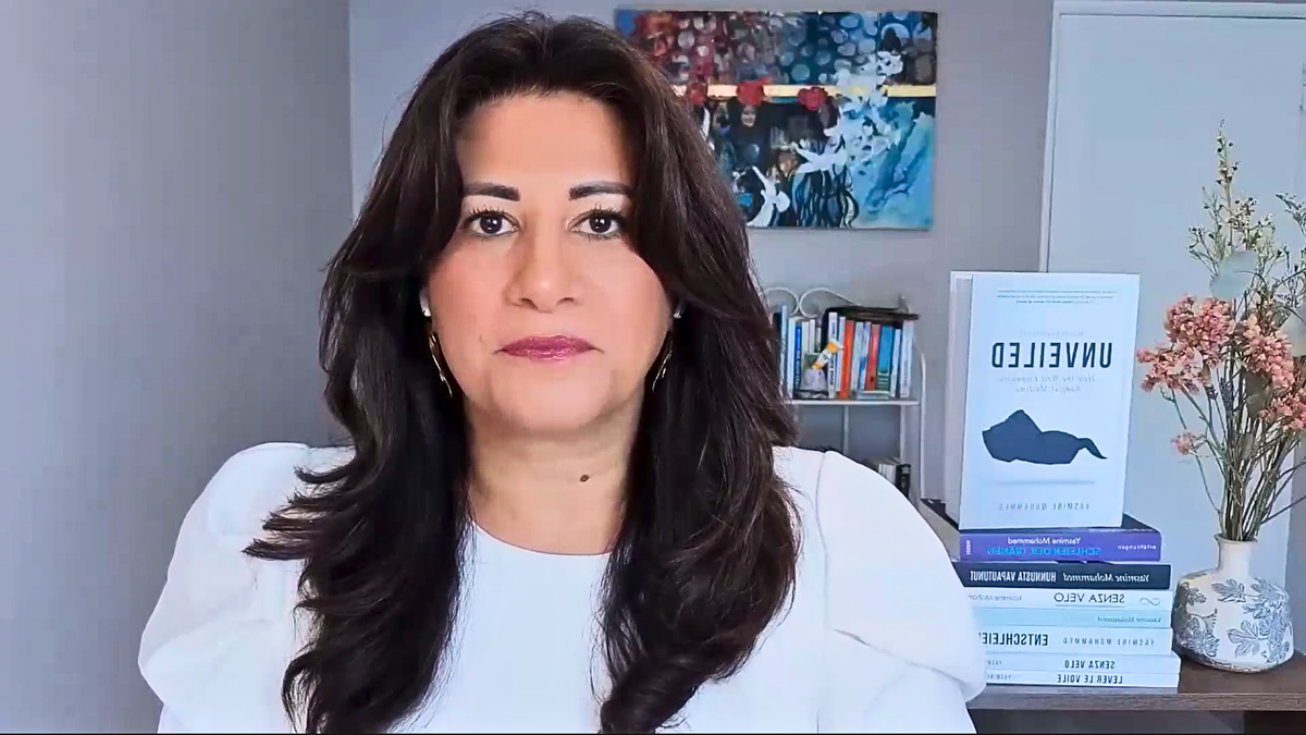 Muslim woman with brown hair and brown eyes faces camera while sitting on desk during interview