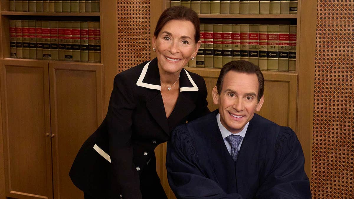 A photo of Judge Judy and son Adam Levy posing behind a desk