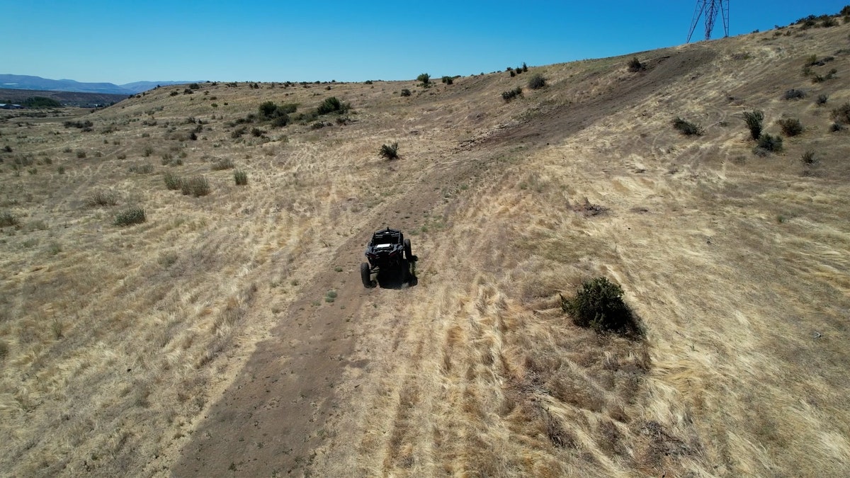 An Overland AI autonomous ground vehicle travels along a dirt trail through dry, hilly terrain in Washington state.
