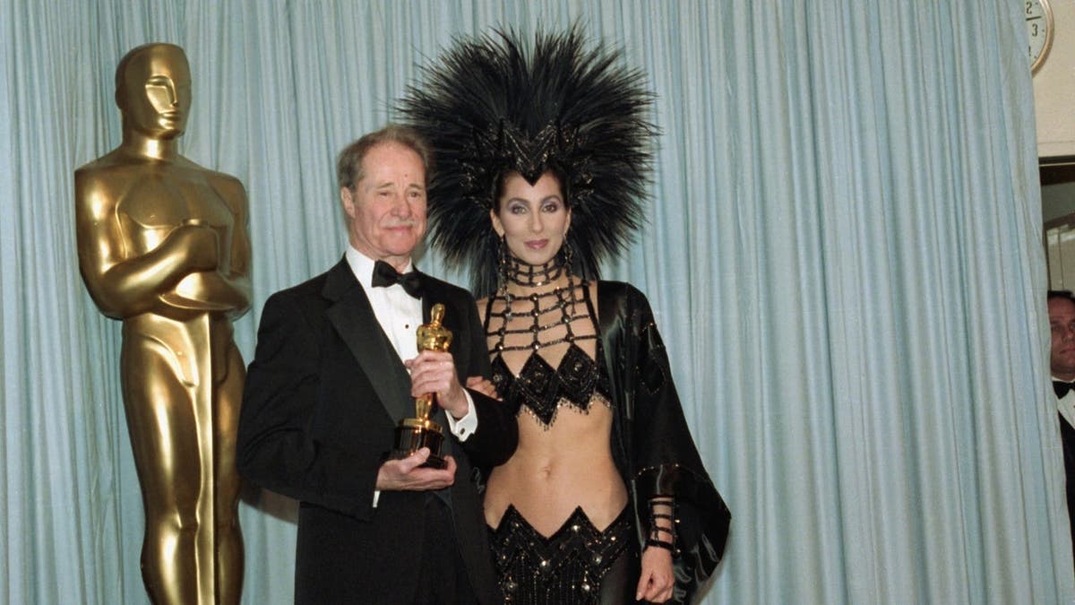 Don Ameche holds his Best Supporting Actor Oscar backstage with Cher beside him.