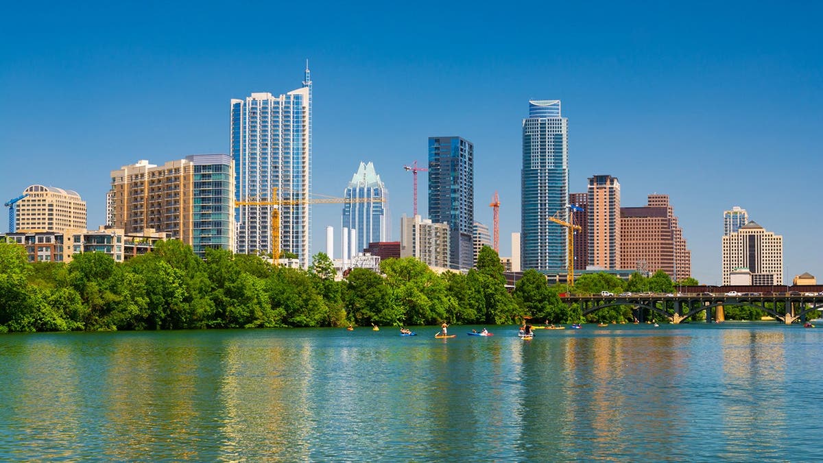 Austin skyline rises behind Lady Bird Lake with canoes, kayaks and paddle boards on the water.
