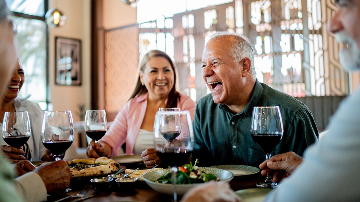 Baby boomers eating and smiling while drinking red wine.