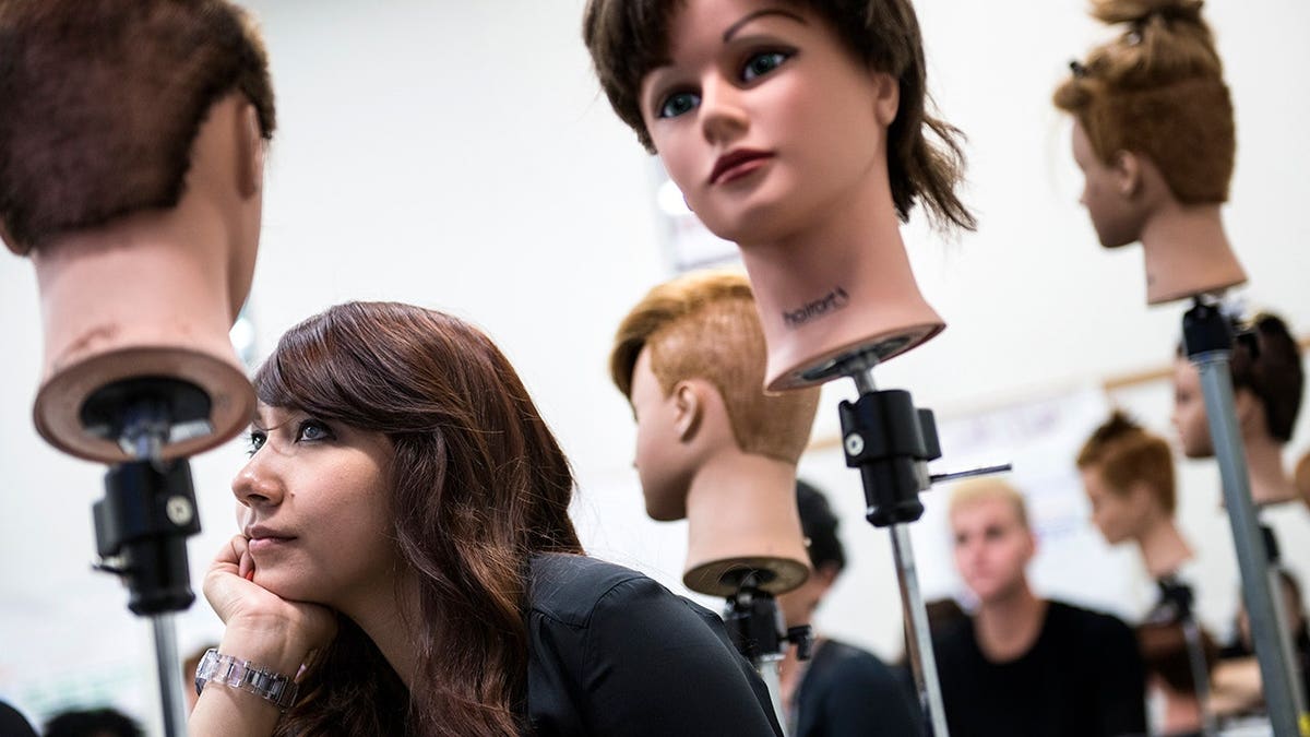 Student watches instructional video beside mannequin heads for hair-cutting practice.