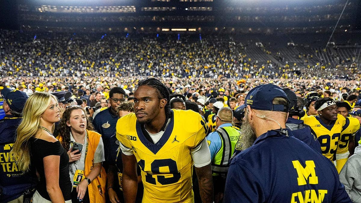 Bryce Underwood, wearing Michigan quarterback jersey number 19, exits the field with Ron Bellamy.