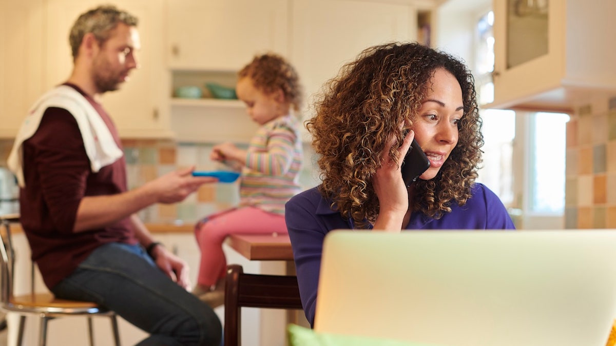 Mom working from home with husband and child in background