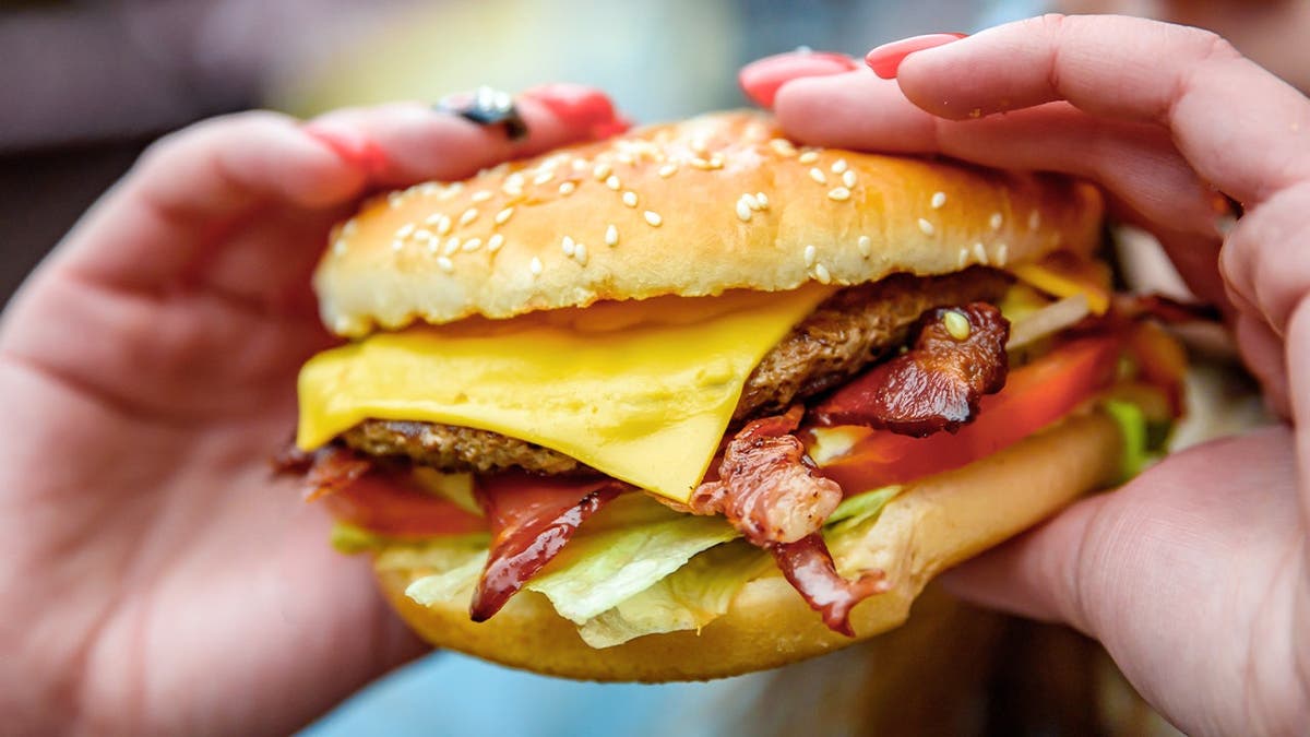 A person takes a bite of a cheeseburger with American cheese.