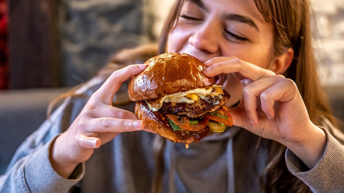 A girl bites into a big cheeseburger.