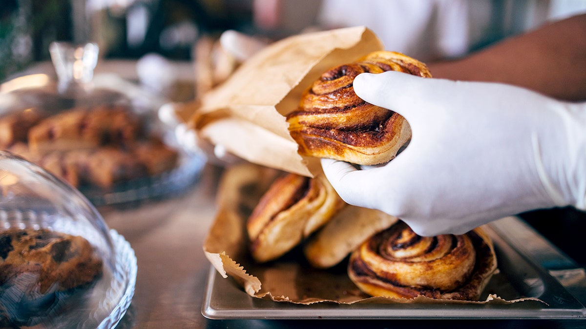 A gloved hand holds a cinnamon roll as it's being placed into a bag.