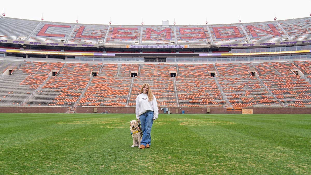 A Canine Companions dog is shown inside Clemson's football stadium with its raiser.