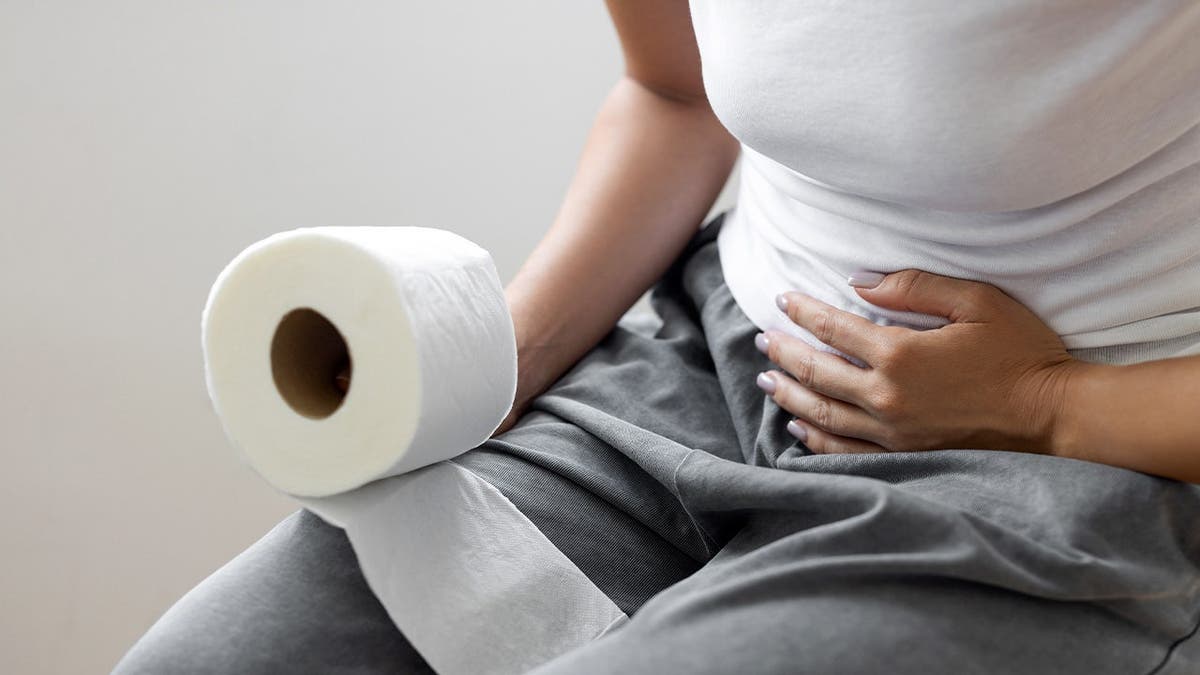 A person grips her stomach and toilet paper.