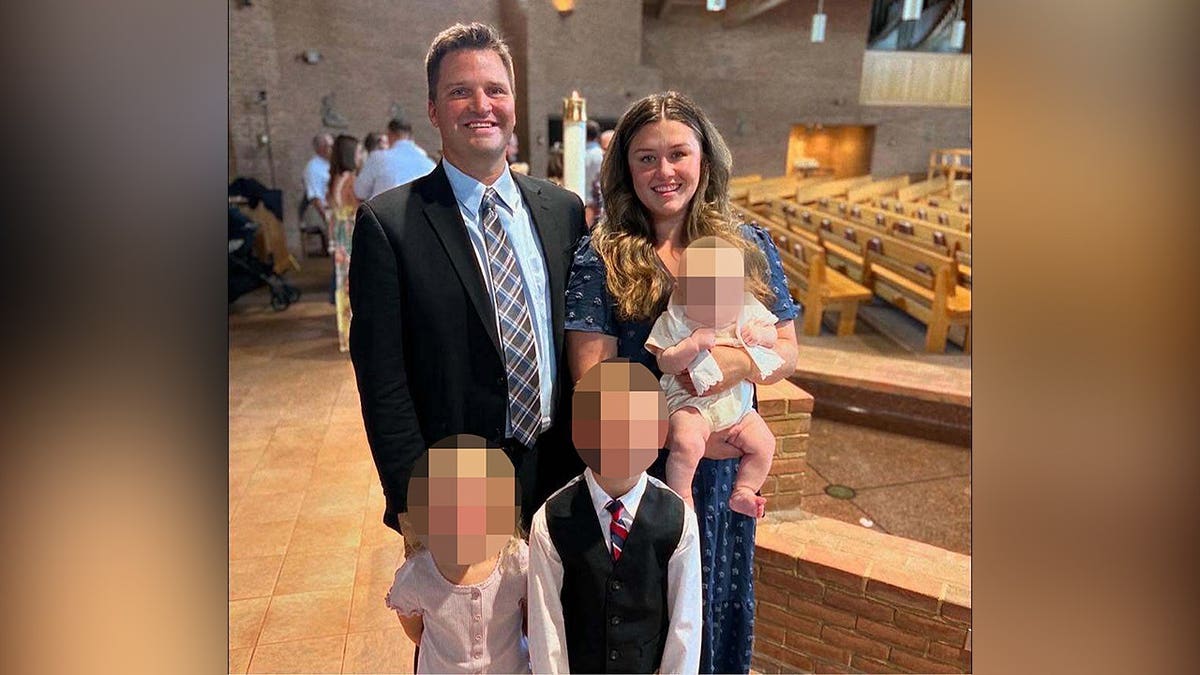 Corie Walsh and her husband standing together inside a church sanctuary with three young children whose faces are blurred.