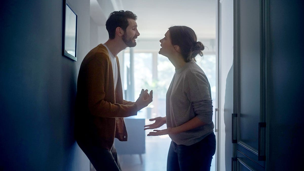 Young couple argues in a dark apartment hallway.