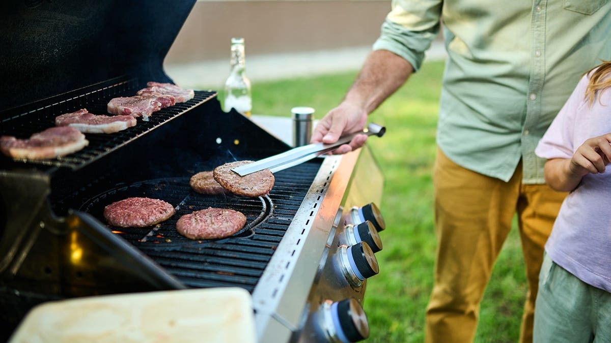 Dad grills burgers and steaks in backyard while kids play nearby.