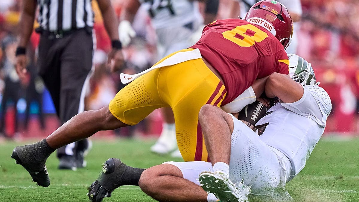 Dante Moore runs with the football and slides to avoid a tackle from Desman Stephens II during a college football game.