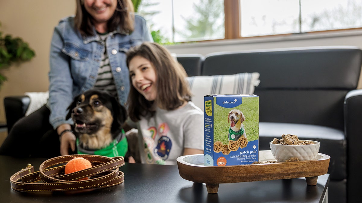 A mother, daughter and their dog are all smiles as they look to the left of the frame.