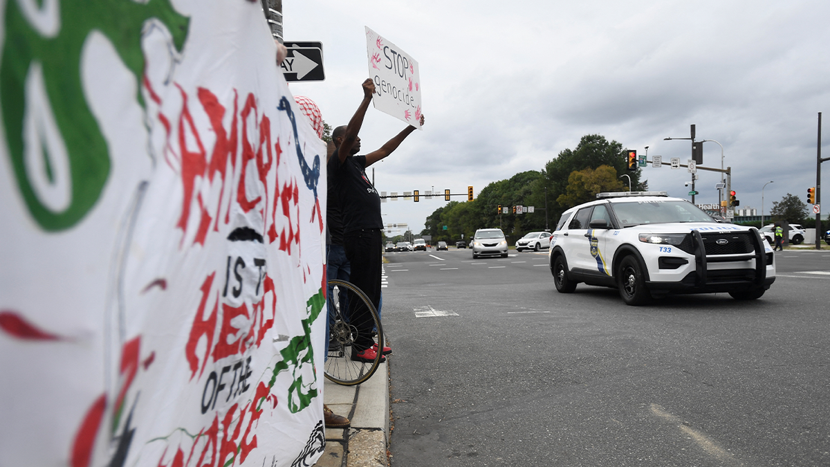 A police car passes pro-Palestinian protesters as they demonstrate near Lincoln Financial Field ahead of Ed Sheeran's concert in Philadelphia, Pennsylvania, on September 19, 2026, following the removal of rapper Macklemore from Sheeran's US tour.