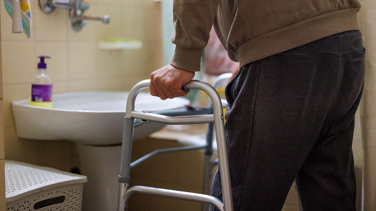 Older man grips a walker in bathroom for support and mobility assistance.