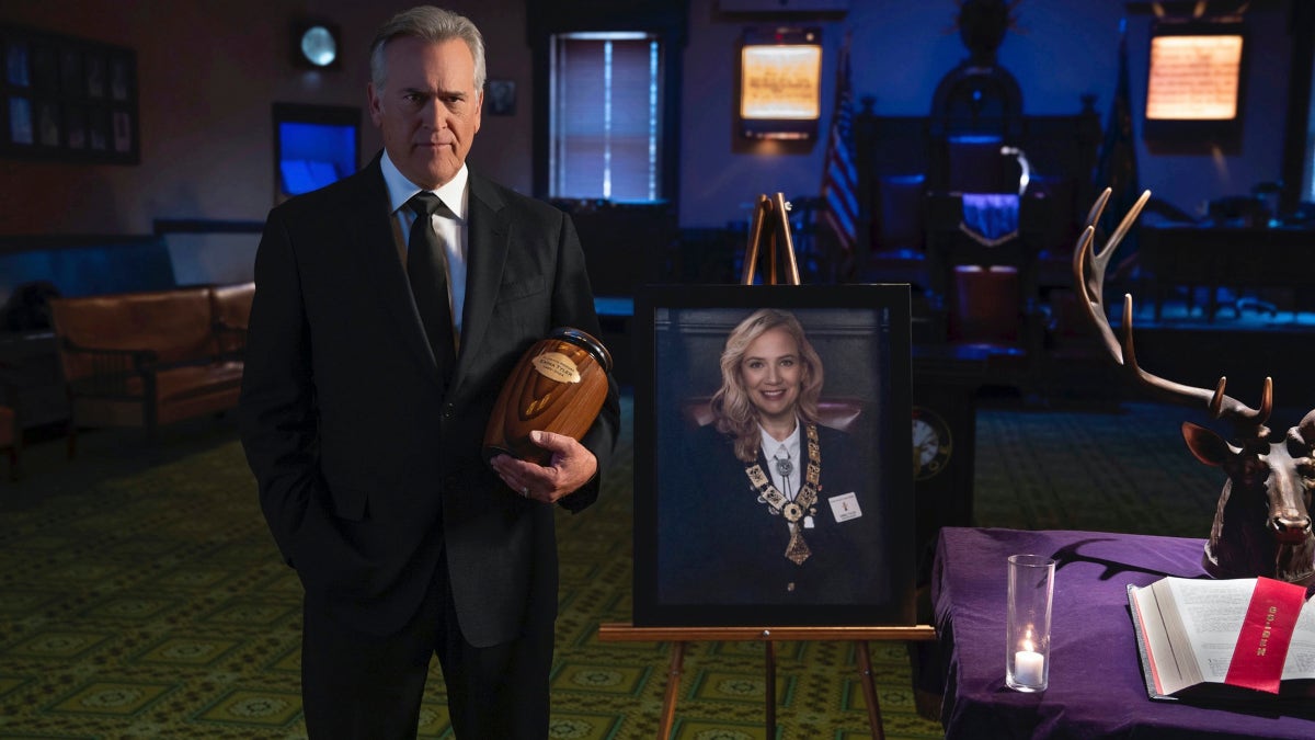 Bruce Campbell holds an urn next to a framed portrait at a memorial service.