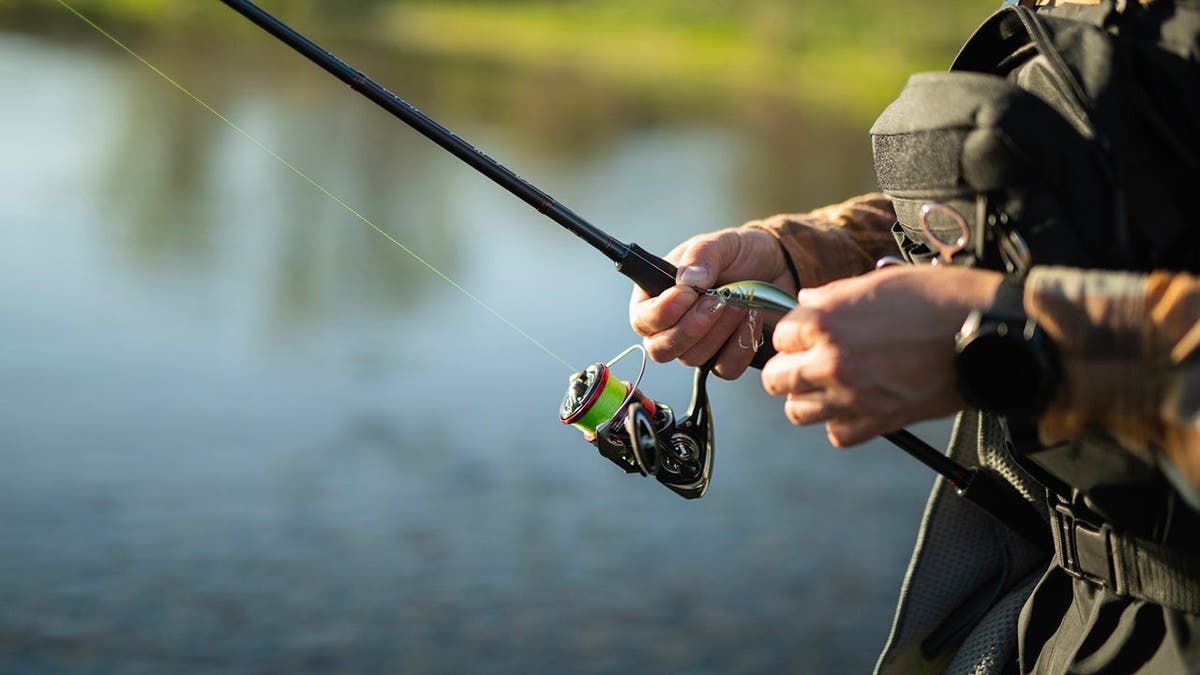 Fisherman prepares bait on a fishing rod at sunset.