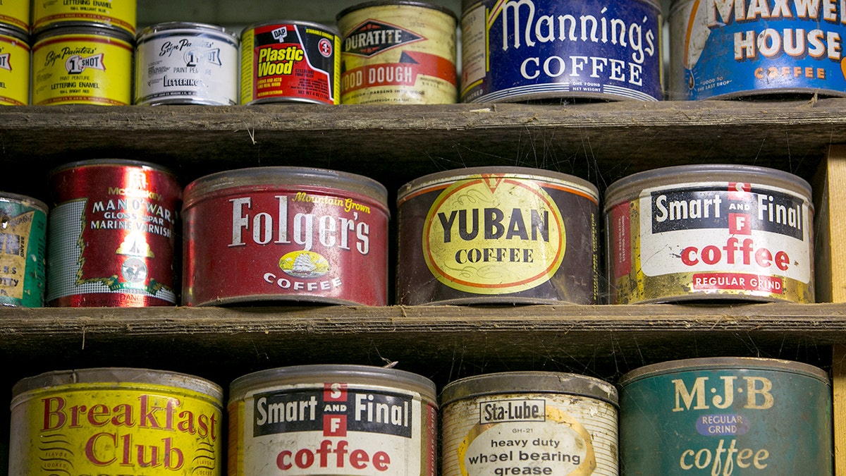 Old coffee cans are displayed on a shelf.