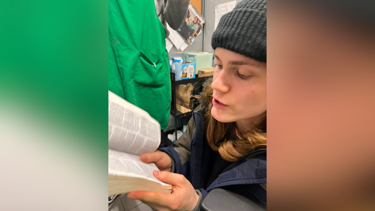 young man in dark beanie with light brown hair reading out of Bible