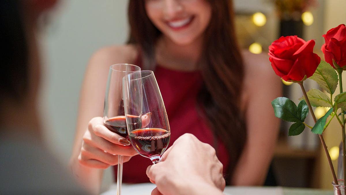 A romantic couple toasts with red wine in a cozy restaurant with warm bokeh lights.