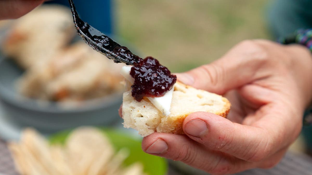 Someone spoons jam on a cracker with goat cheese.