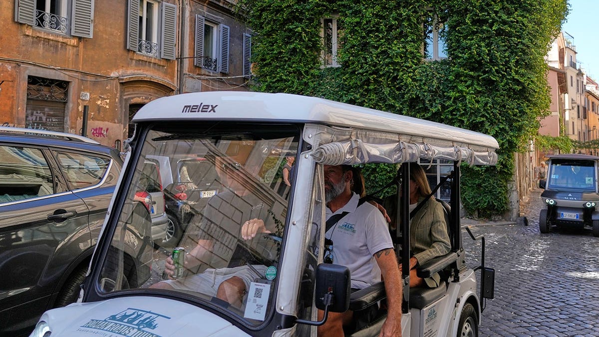 A golf cart carrying tourists travels through a Rome street.