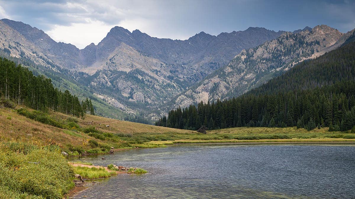 Alpine lake with jagged granite peaks of the Gore Range under storm clouds in Colorado.