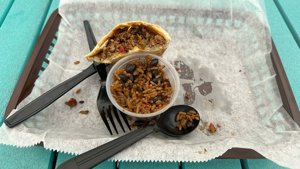 A half-eaten beef empanada with rice on a tray.