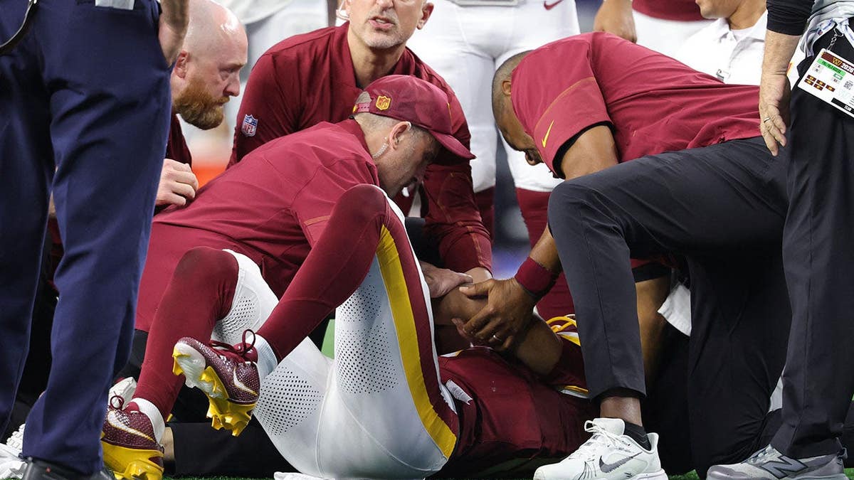 Jayden Daniels lies on the field with an apparent left arm injury during an NFL game.