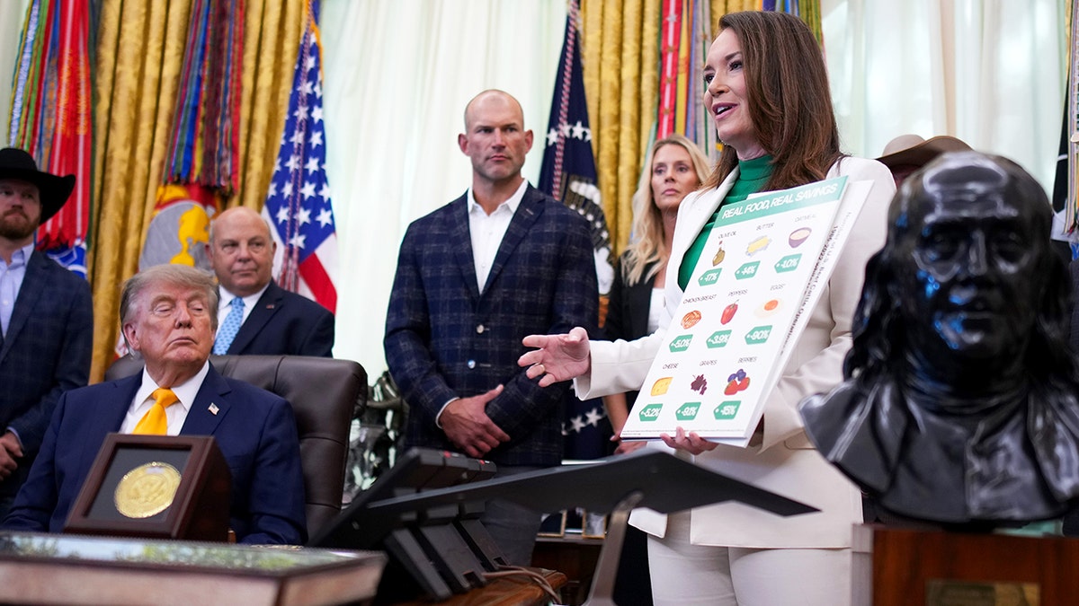 Joe Thomas and President Donald Trump look as Brooke Rollins holds a poster board titled "Real Food, Real Savings."
