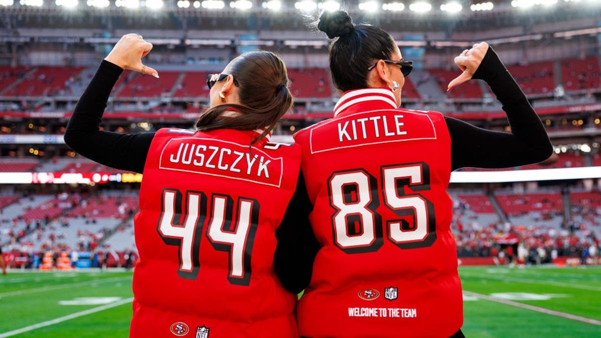 Kristin Juszczyk and Claire Kittle pose wearing Offseason vests at State Farm Stadium.