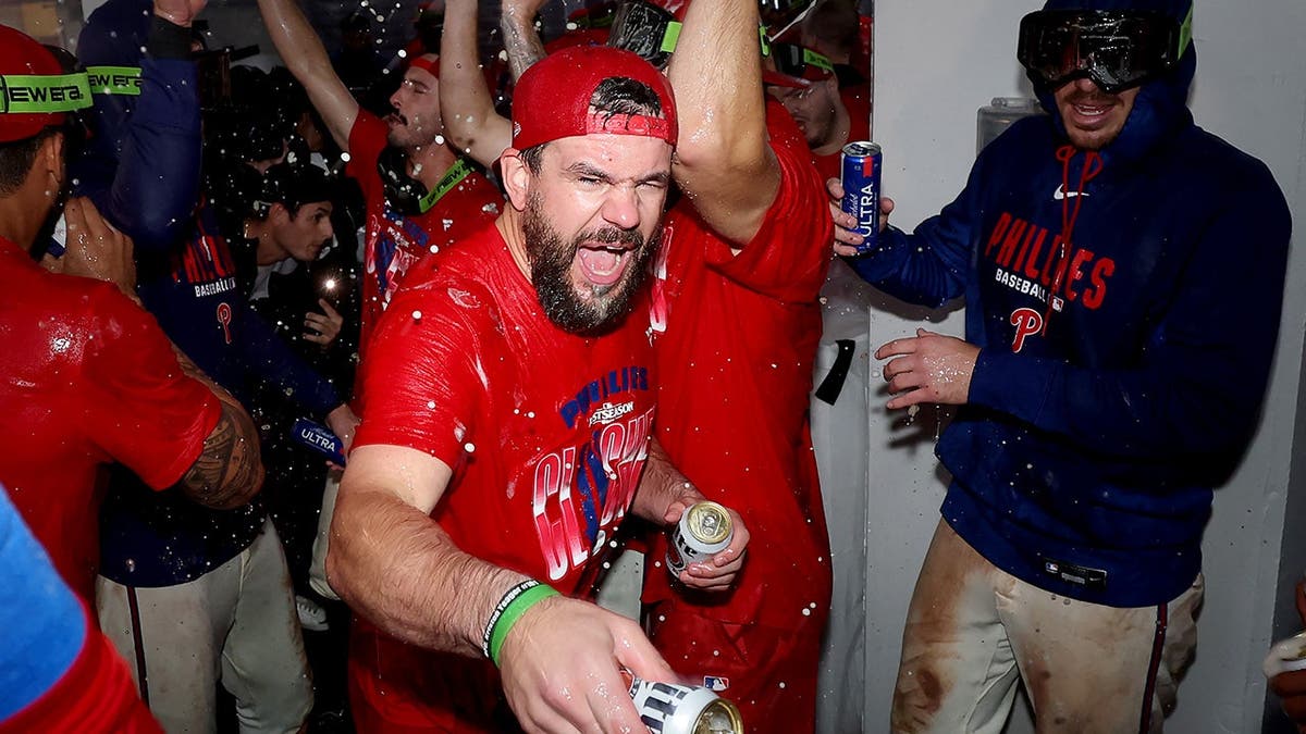 Kyle Schwarber and Bryson Stott celebrate with Philadelphia Phillies teammates in a clubhouse.