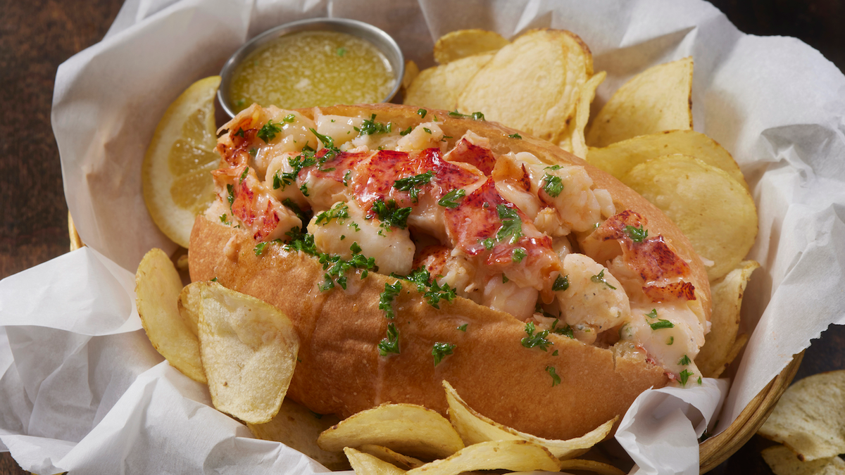 A lobster roll served with melted butter and crispy potato chips.
