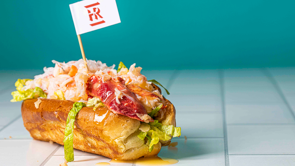 A lobster roll with lobster, lettuce, and condiments against a blue background